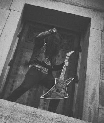 Promo photo: guitarist with a Kelly-style guitar in front of a crypt door